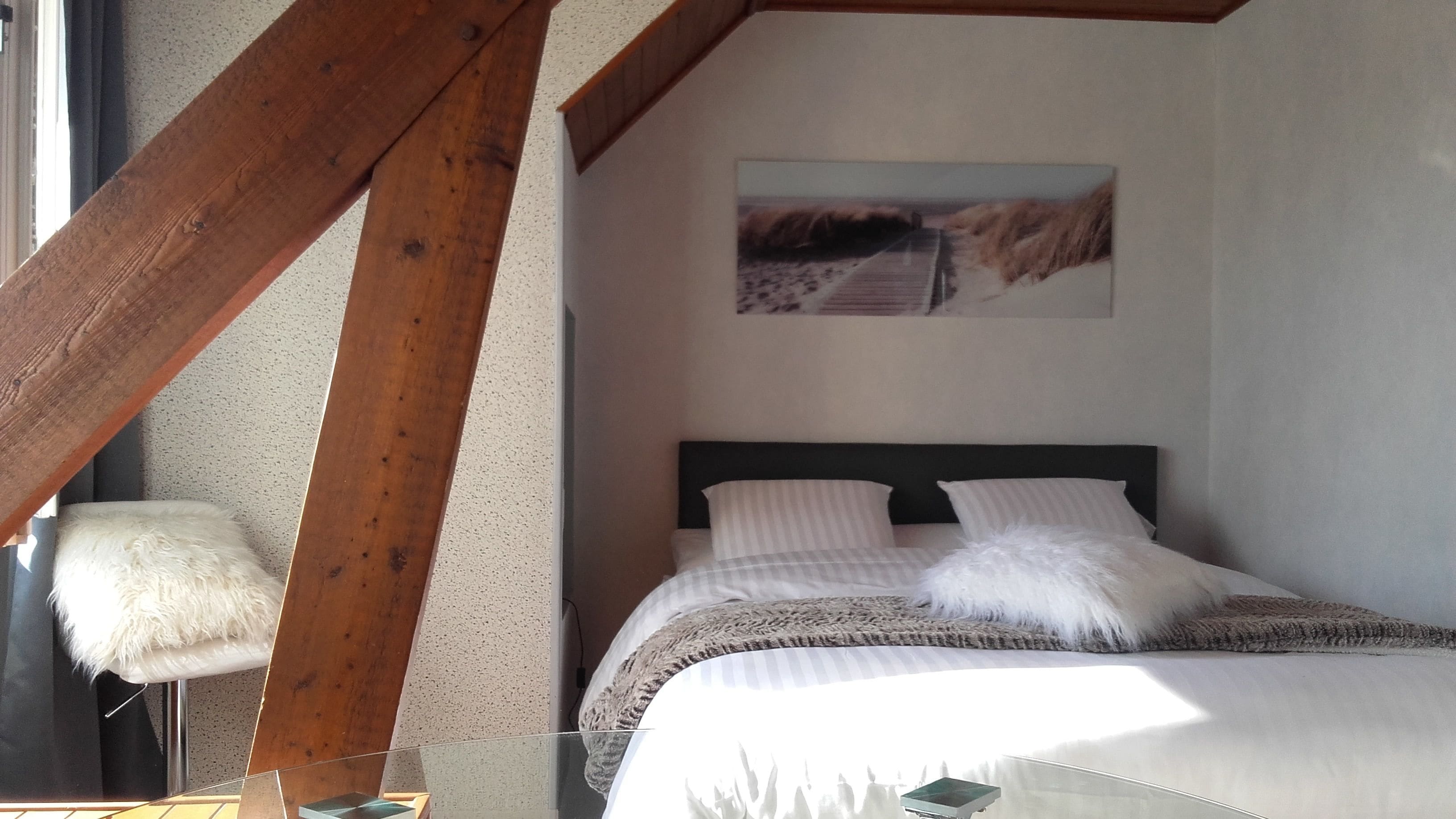 Una camera da letto con un letto, un trave in legno a soffitto, un quadro appeso al muro e una poltrona soffice.