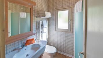 Baño con lavamanos, inodoro y espejo. Hay un perchero sobre el inodoro y una ventana en la pared.