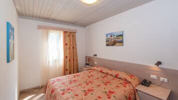 A bedroom with a bed, a nightstand, a lamp, a painting, and a window with curtains.