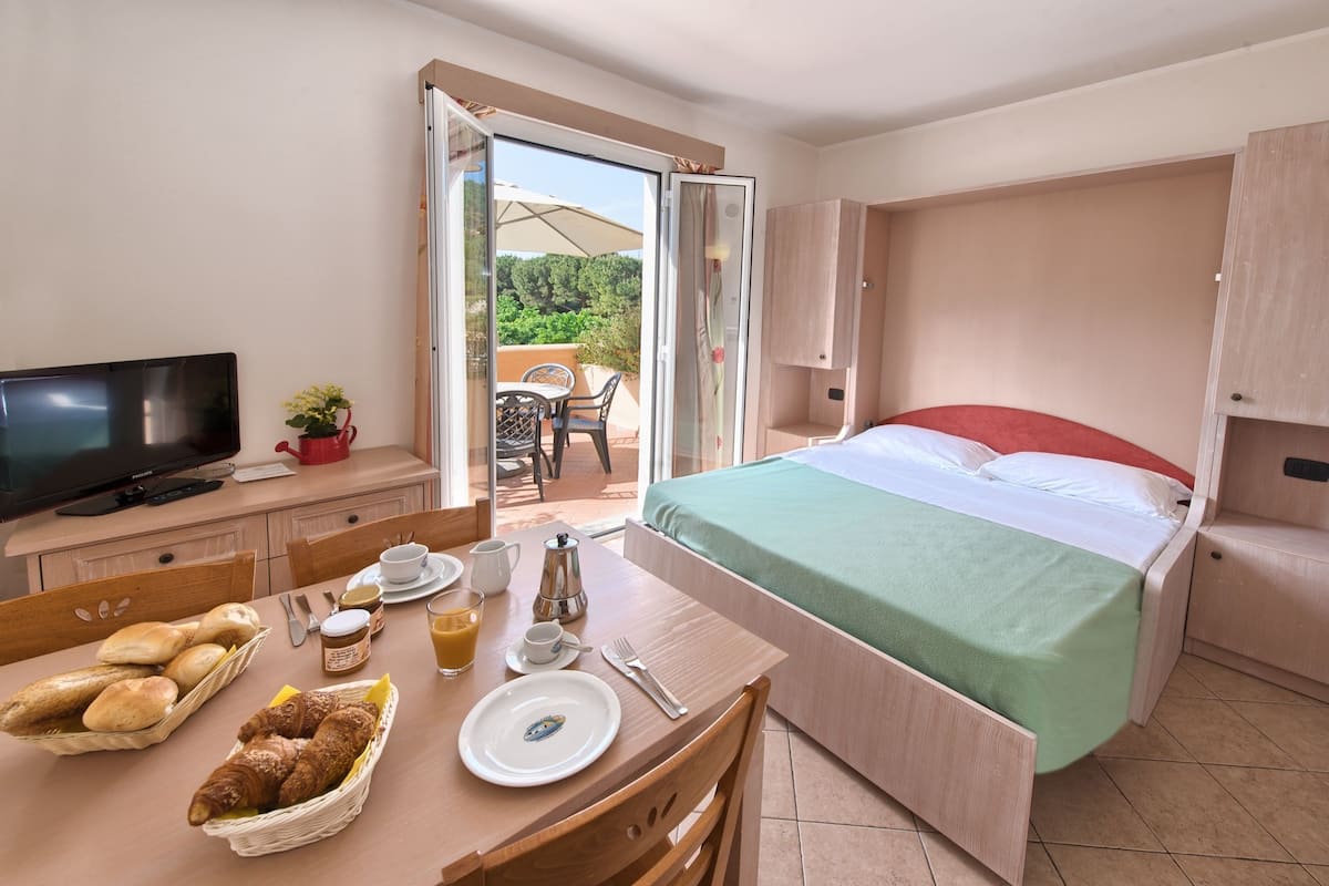 A hotel room with a bed, breakfast setup, and an open door to an outdoor area.