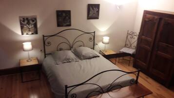 A bedroom with a metal bed frame, two bedside tables with lamps, a wooden bench, and three framed pictures on the wall.
