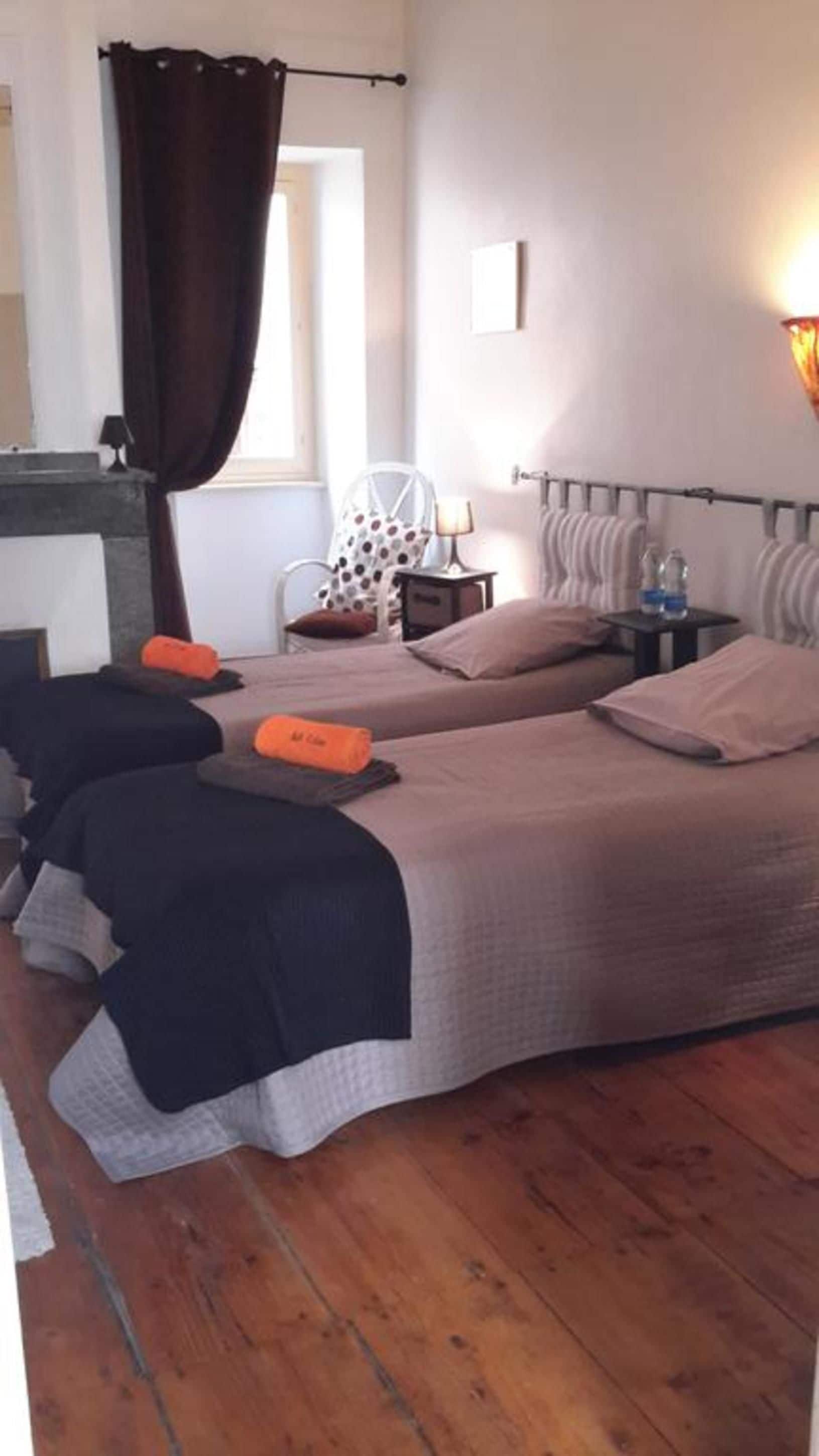 Habitación de hotel con dos camas, una mesita con lámpara, una silla y una ventana con cortinas.