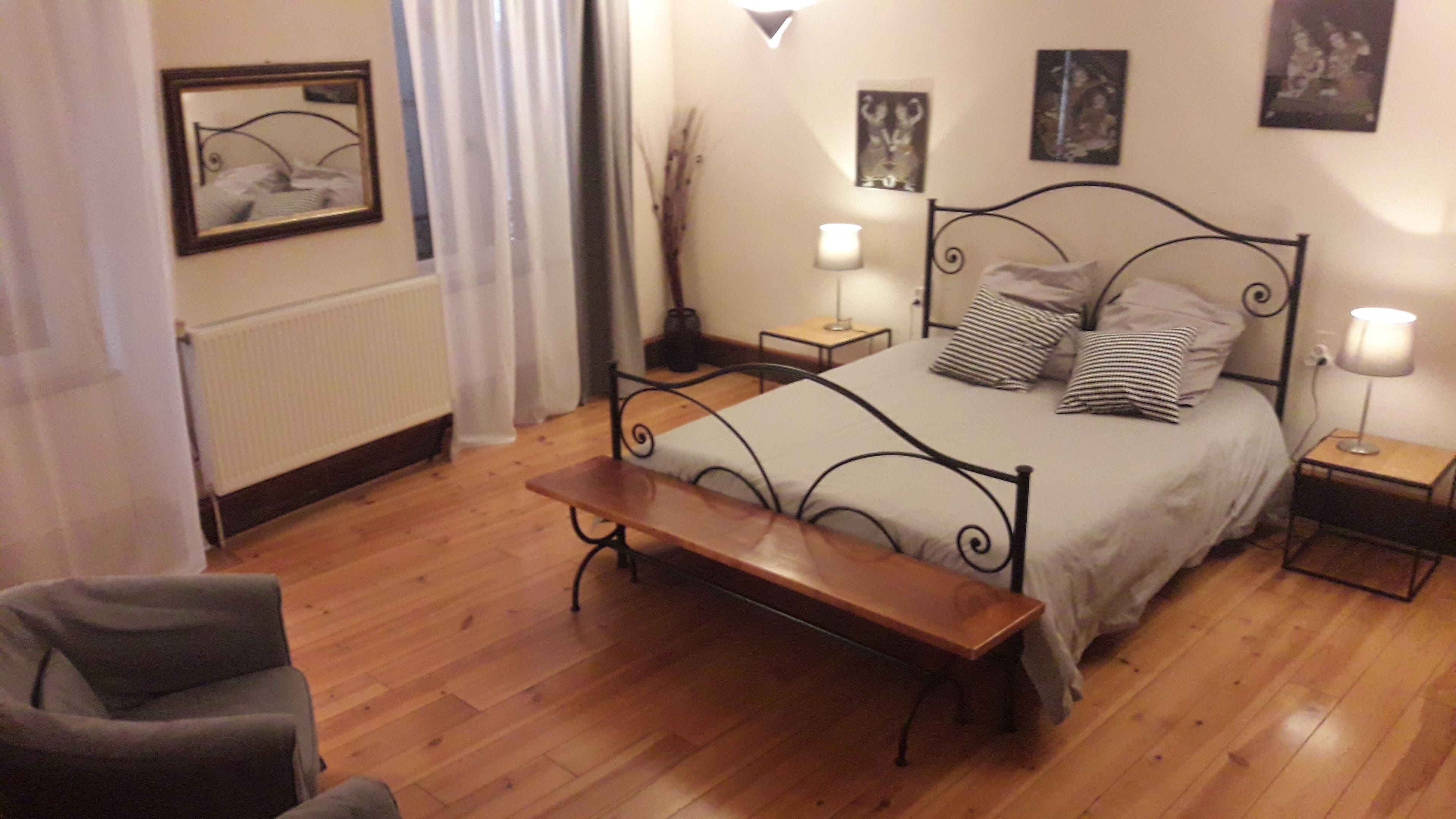 A bedroom with a bed, bedside tables, a bench, a chair, and a radiator.