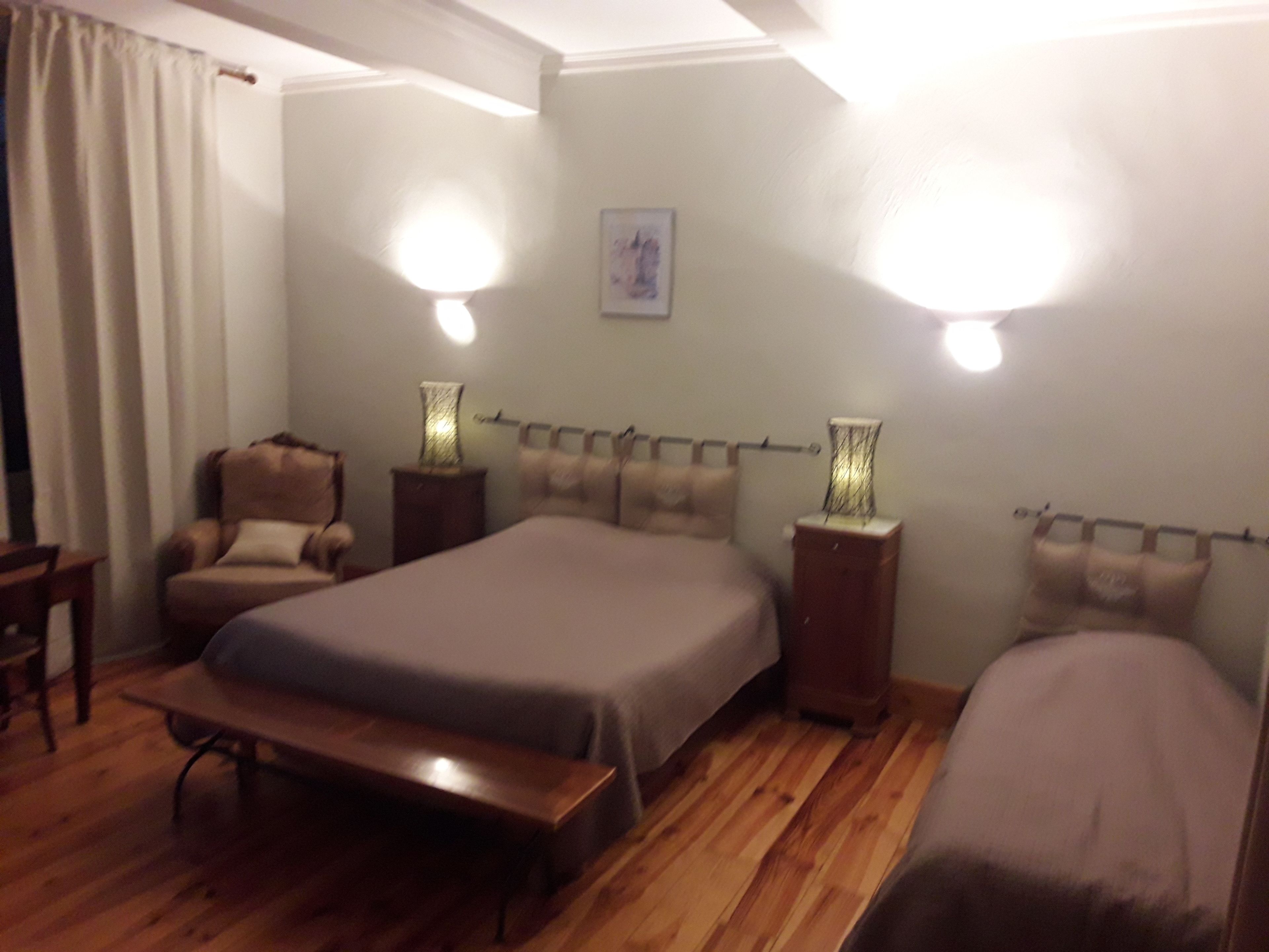 A bedroom with a bed, two bedside tables, a chair, a bench, and two wall-mounted lamps.