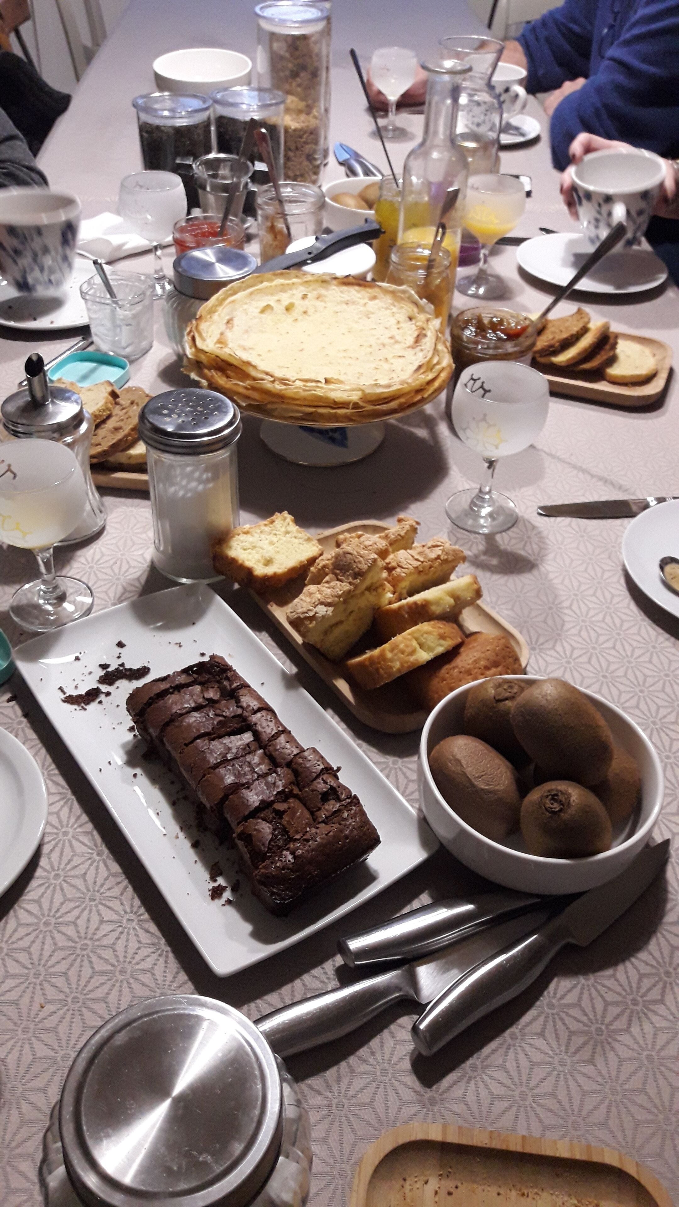 A table set with various dishes including a pie, biscuits, brownies, and a bowl of kiwis.