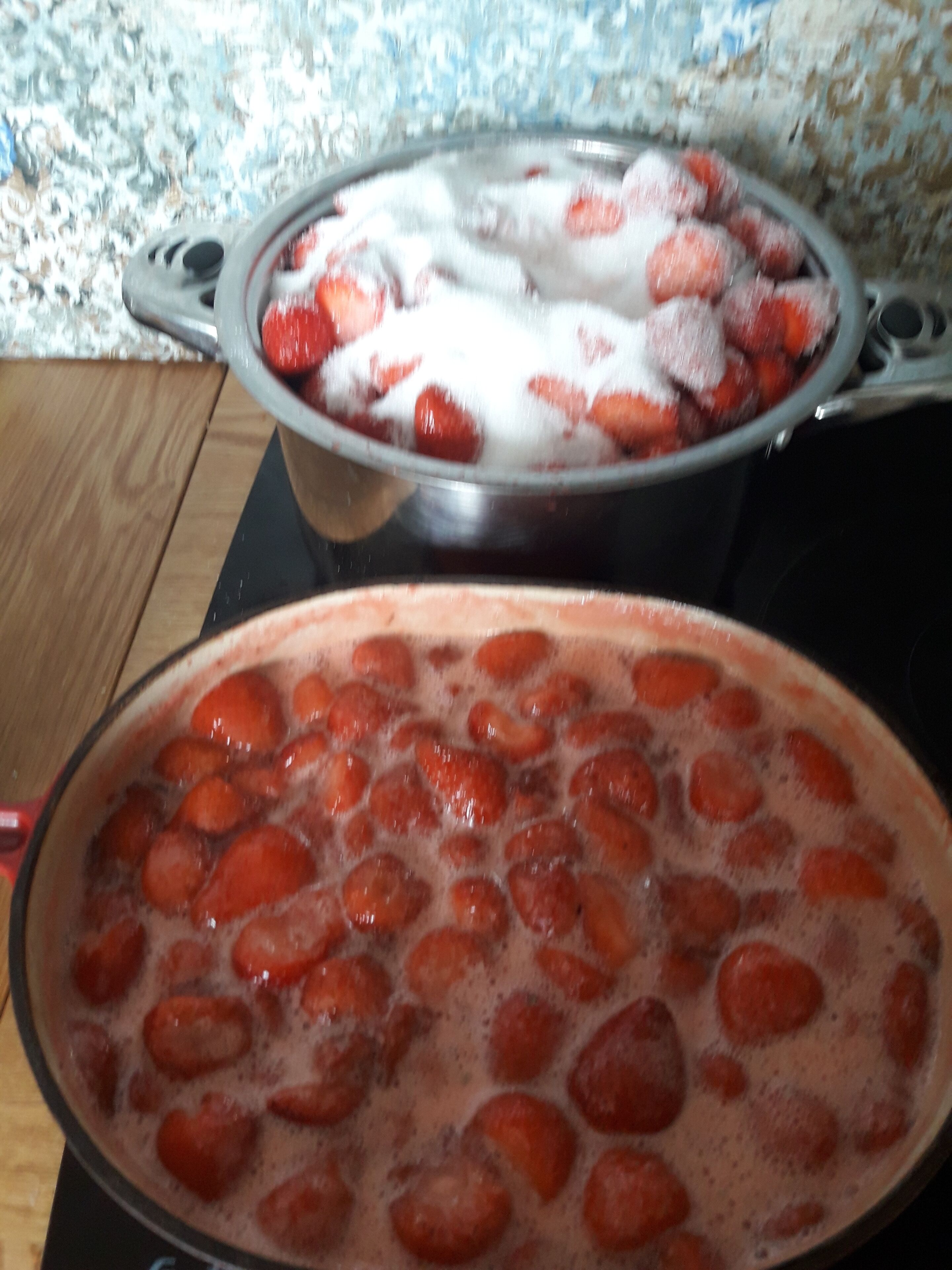 Eine Küche mit einem Topf Erdbeeren, die auf dem Herd köcheln, und einem weiteren Topf Erdbeeren mit Zucker.