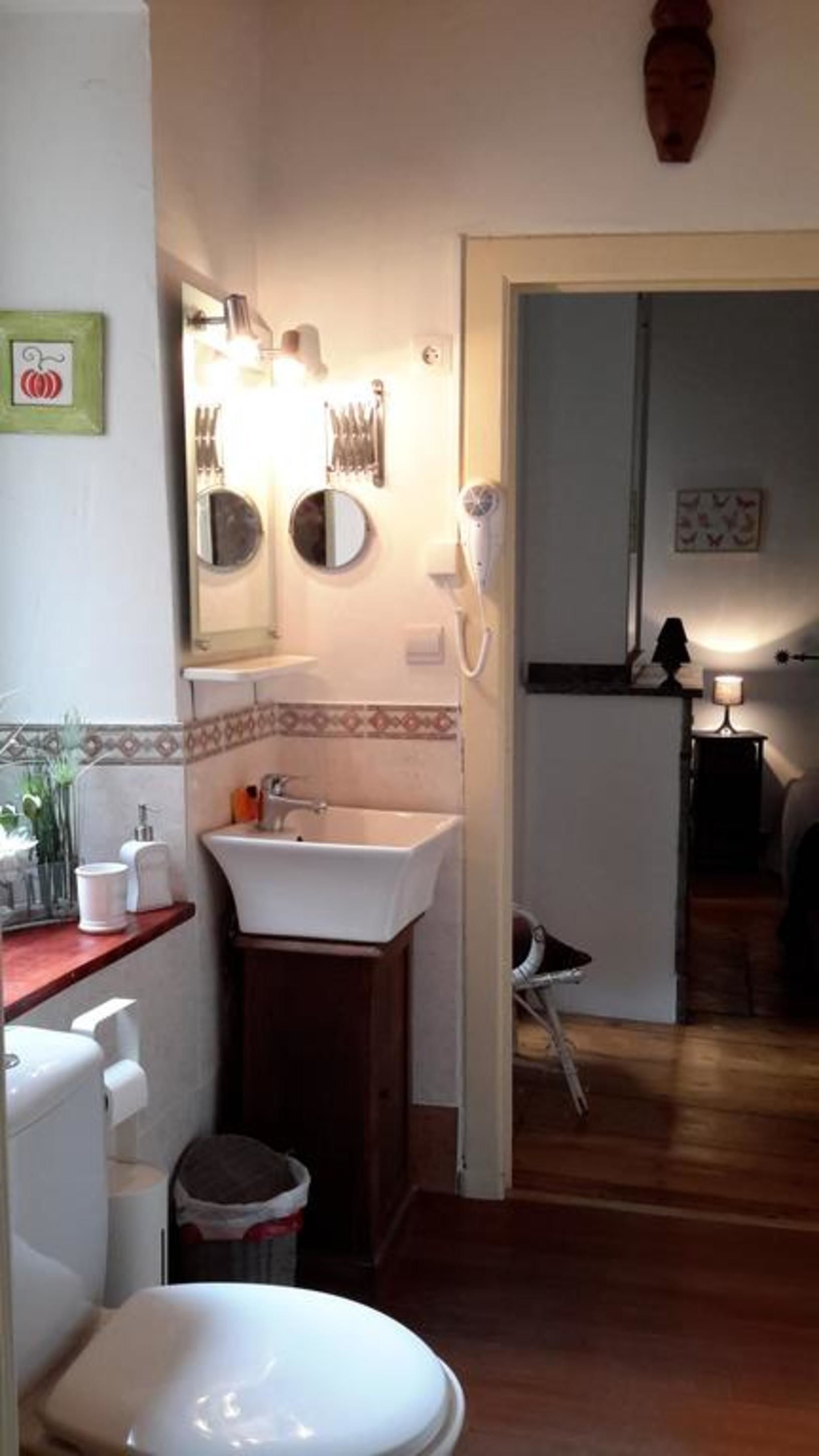 A bathroom with a sink, mirror, and toilet. There is a towel rack above the sink and a small trash bin next to the toilet.