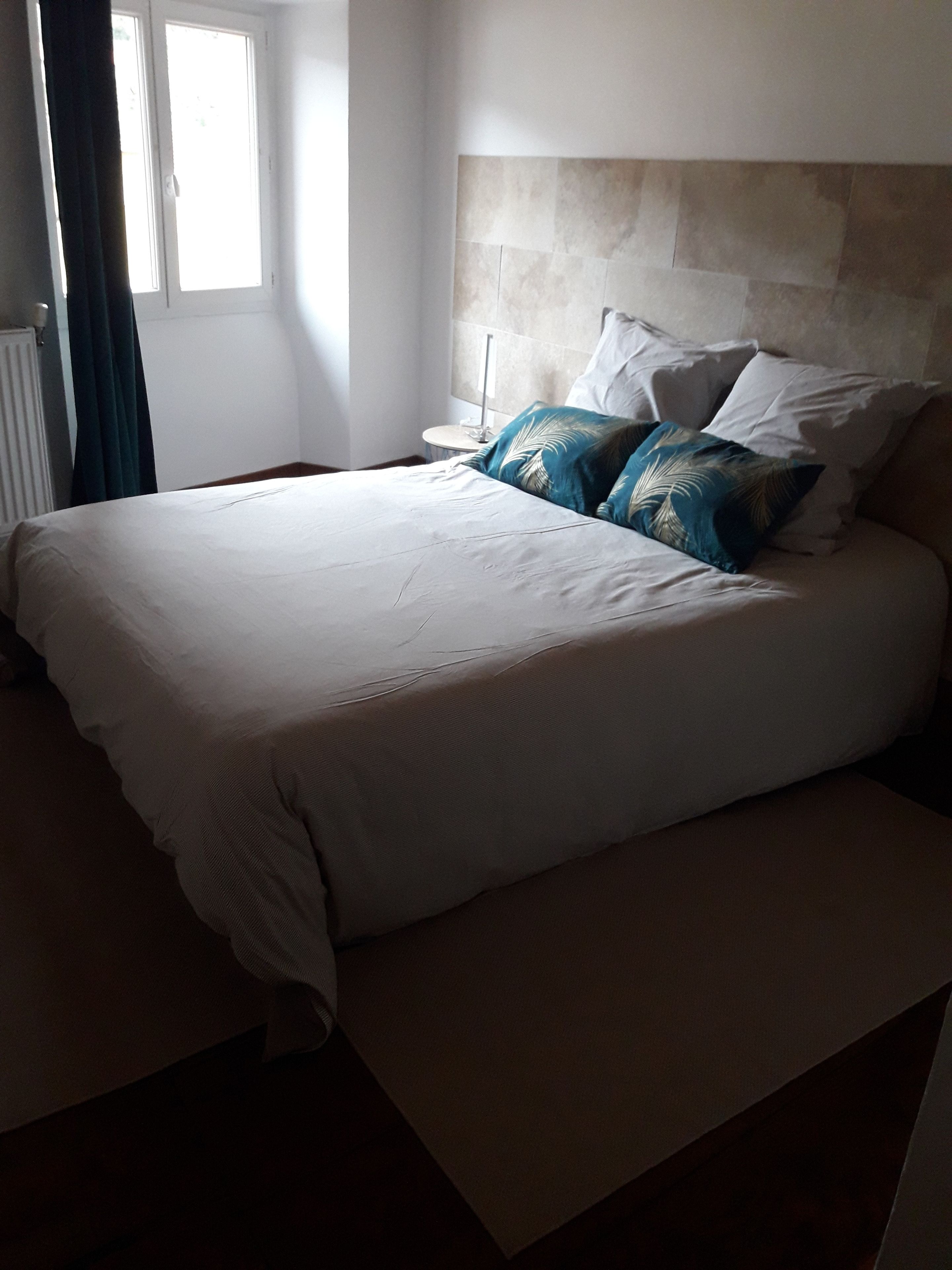 Un lit bien fait, avec une tête de lit, une table de chevet et une fenêtre avec des rideaux.