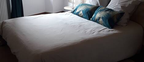 Un lit bien fait, avec une tête de lit, une table de chevet et une fenêtre avec des rideaux.