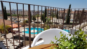 Un balcón con vista a una piscina, sillas de descanso y una mesa de madera.