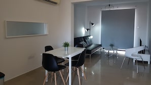 Una sala de estar moderna con comedor, que incluye un sofá, sillas, una mesa de centro y un televisor.