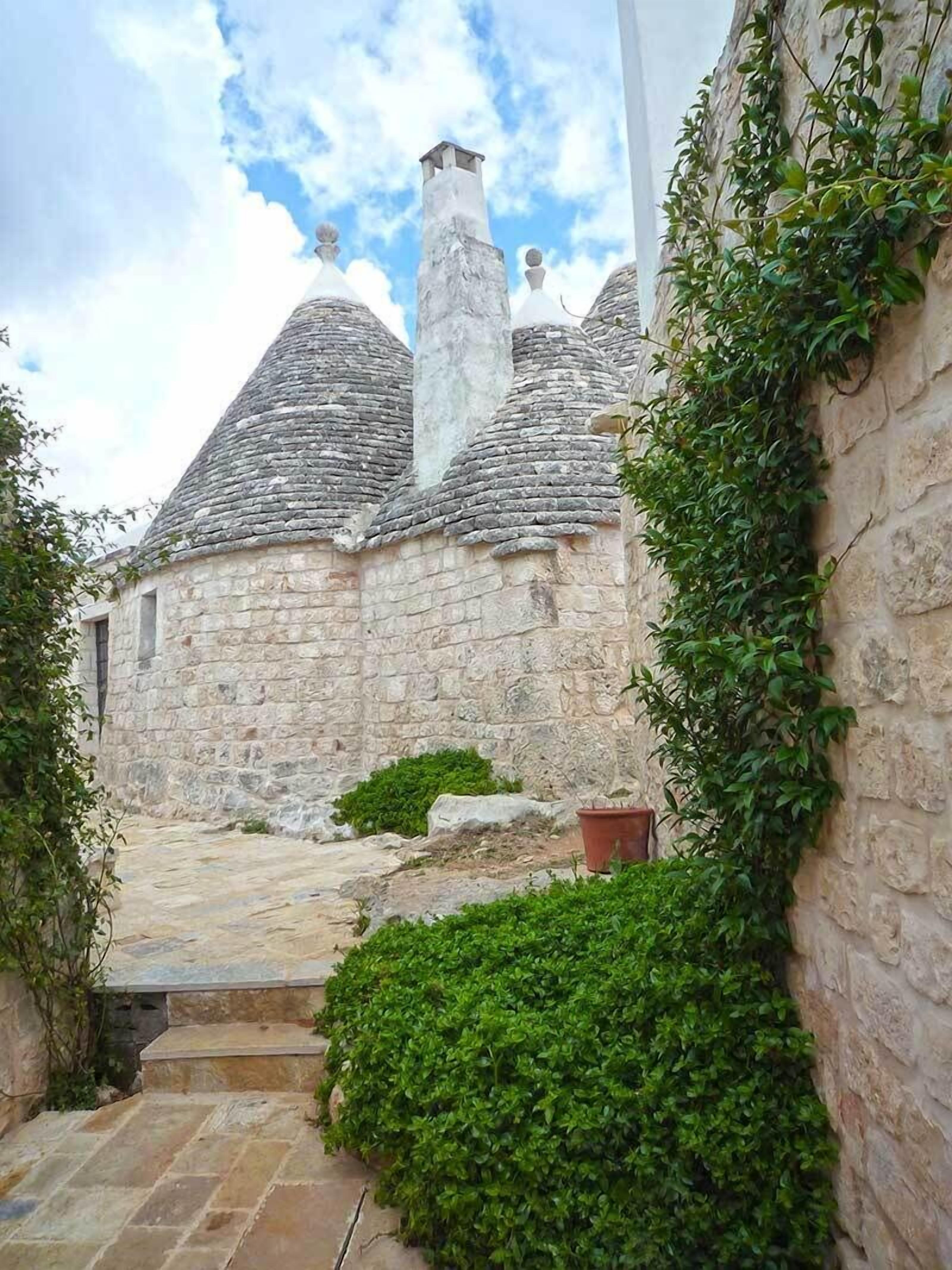 Um edifício de pedra com telhado íngreme, chaminé e uma escadaria de pedra estreita que leva a uma porta.