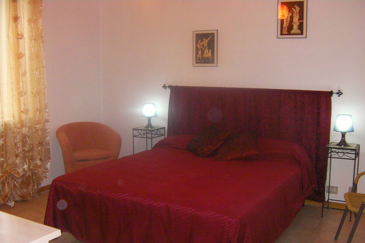 Un dormitorio con una cama grande, dos mesitas de noche con lámparas, una silla y una cortina.