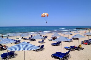 Ein Strand mit Reihen aus blauen und weißen gestreiften Sonnenschirmen und Liegestühlen.