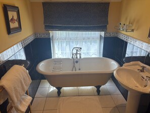A bathroom with a freestanding bathtub, a sink, a towel rack, and a window with a curtain. - Hunters Rest Inn (Bristol)