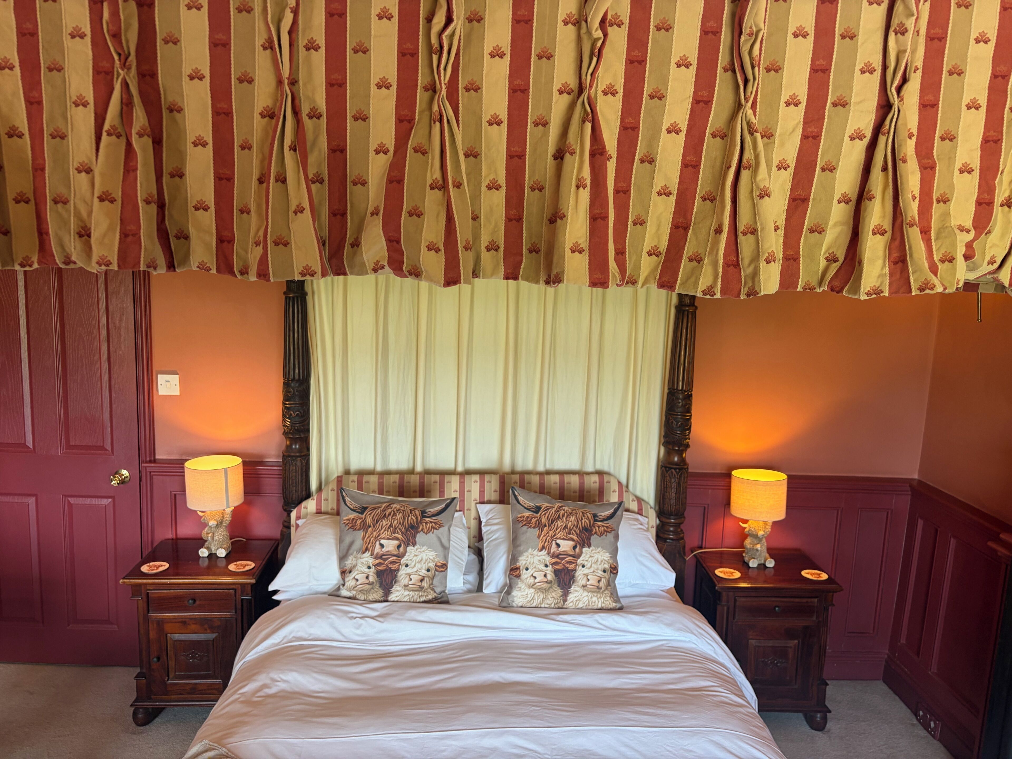 A hotel room with a bed, two bedside tables with lamps, a headboard with a floral pattern, and a curtain with a striped pattern.