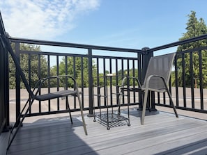 A deck with two chairs and a table, surrounded by a black railing, overlooking a road and greenery. - Hunters Rest Inn (Bristol)