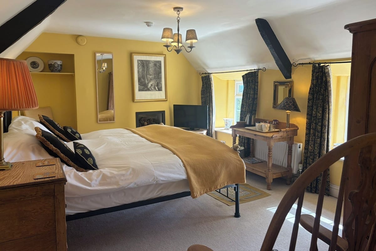 A bedroom with a bed, bedside table, lamp, and a desk with a chair.