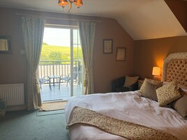 A bedroom with a large bed, a balcony with chairs, and a view of the outdoors.