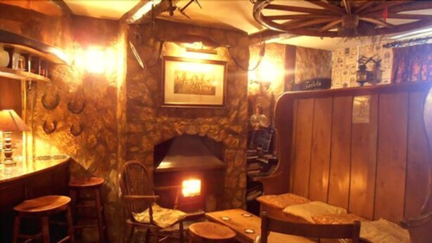 Un intérieur rustique avec un mur en pierre, une cheminée, des meubles en bois et un coin bar.