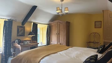 Un dormitorio con cama, armario de madera, escritorio con lámpara, silla y ventana con cortinas.