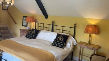 A bedroom with a bed, two bedside tables, a chair, a lamp, a picture frame, and a chandelier.