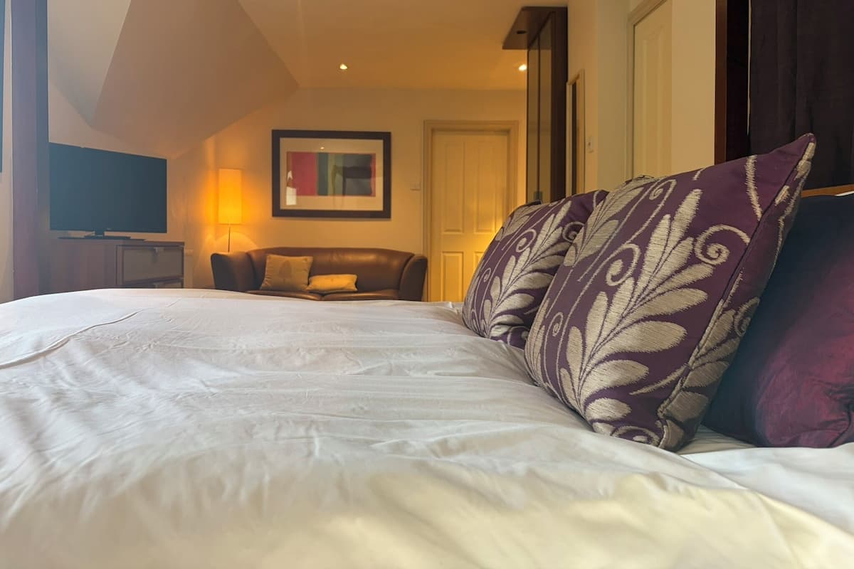 A hotel room with a bed, a television, a sofa, and a painting on the wall.