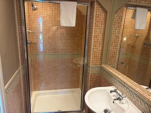 A bathroom with a glass-enclosed shower, a white sink, and a tiled wall.