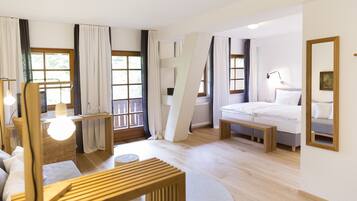 A modern hotel room with a wooden bed, a bedside table, a lamp, a wicker chair, and a large window with curtains.