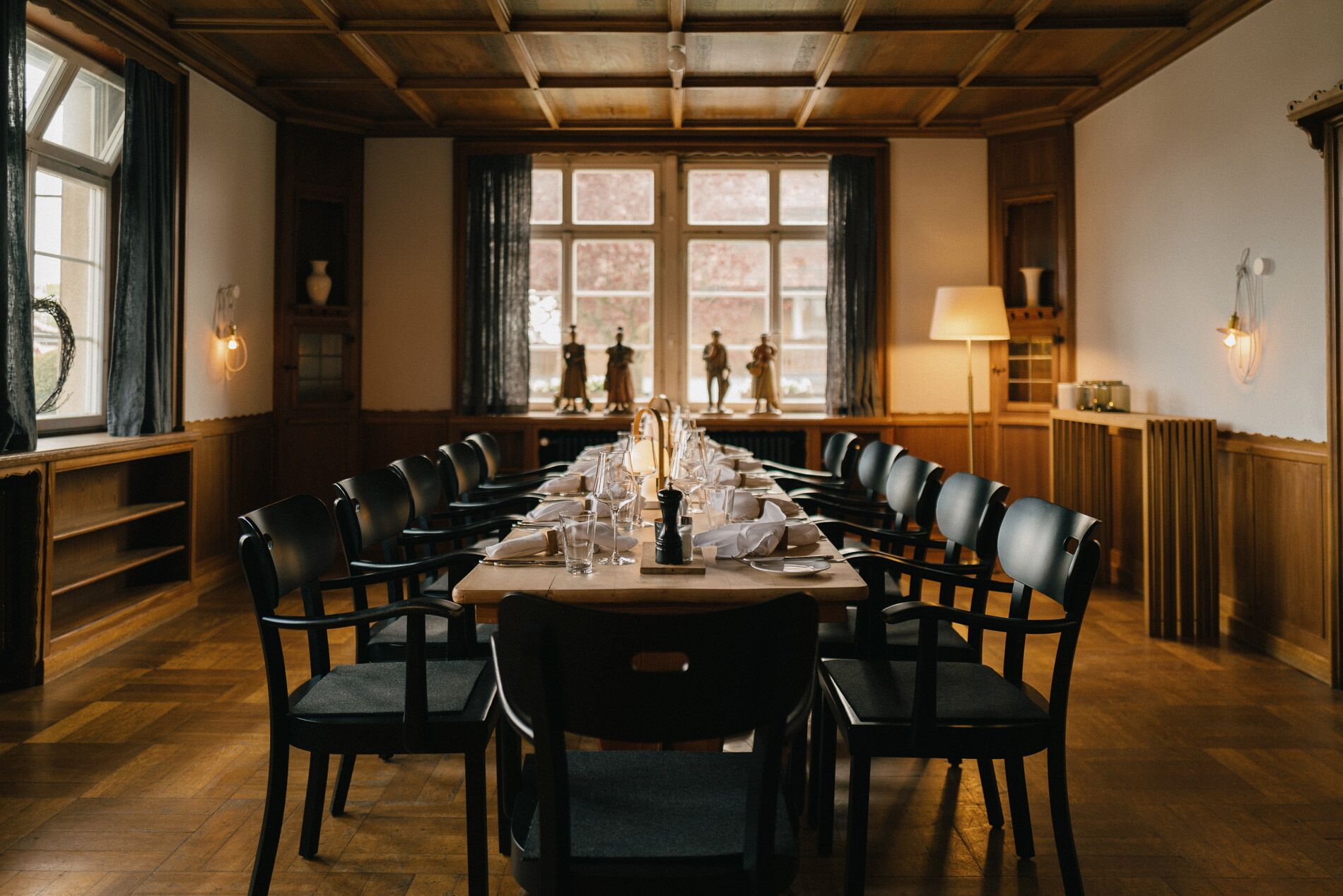 Un comedor con una larga mesa dispuesta para una comida, paredes revestidas de madera y vistas a través de las ventanas.