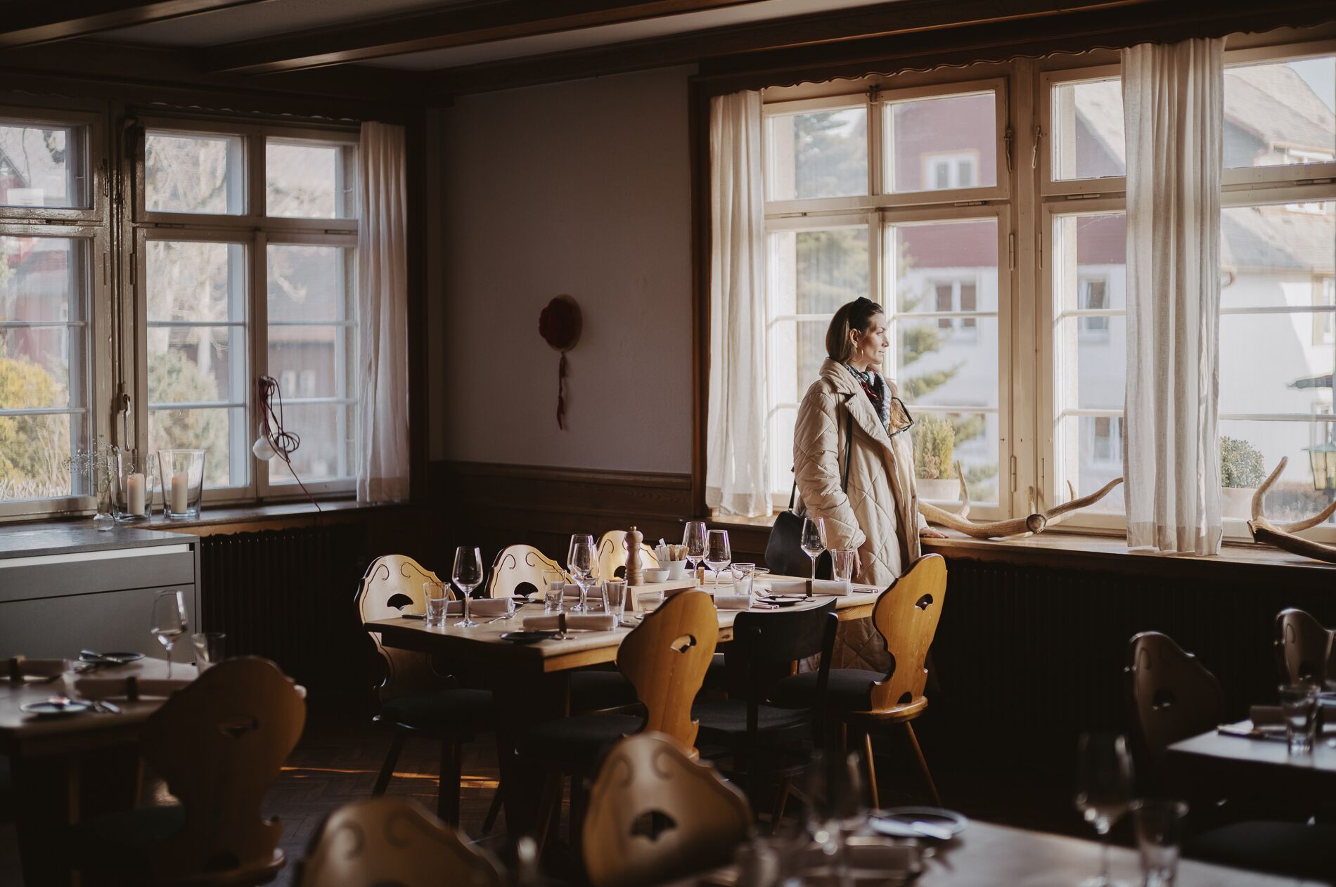 A dining area with a table set for a meal, a person standing by the window, and a view of the outside.