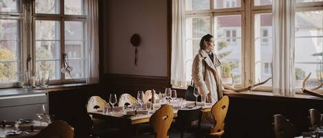 Comedor con una mesa lista para comer, una persona de pie junto a la ventana y vistas al exterior.