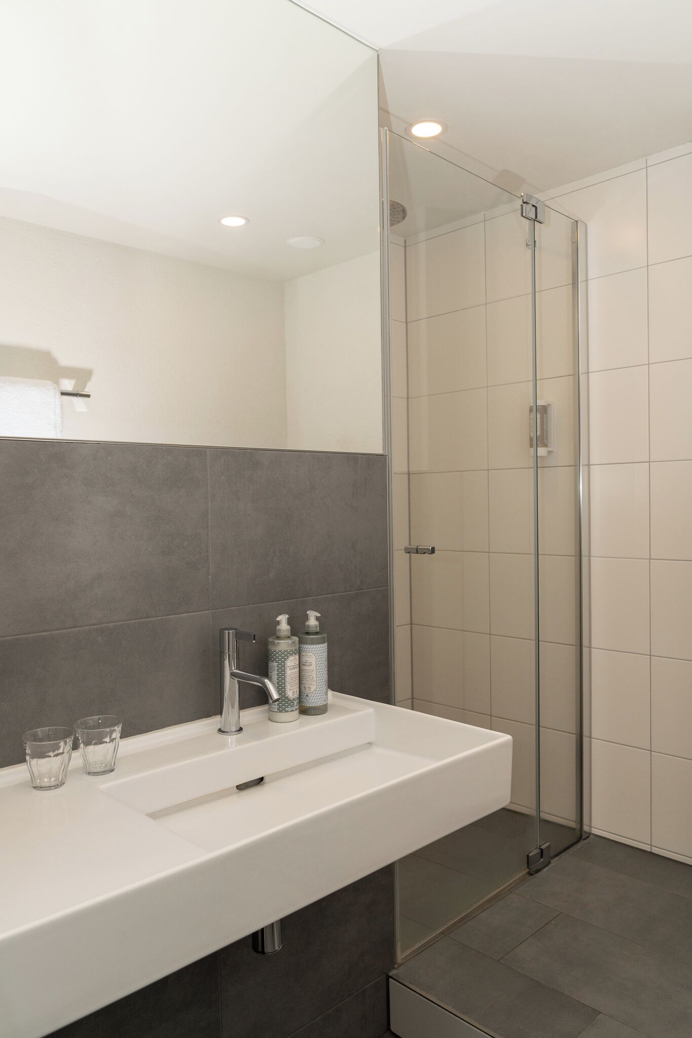 A modern bathroom with a white sink, two glass cups, and two bottles of shampoo and conditioner.