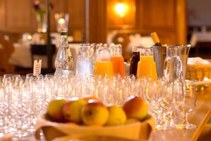 A table with multiple glasses and bottles of beverages, a bowl of fruit, and a bottle of water. - Der Hirschen (Sankt Maergen)
