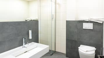 A modern bathroom with a glass-enclosed shower, a white sink, and a toilet.