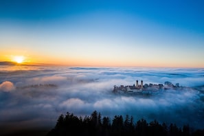 A town nestled among clouds with a clear sky and a sunrise. - Der Hirschen (Sankt Maergen)