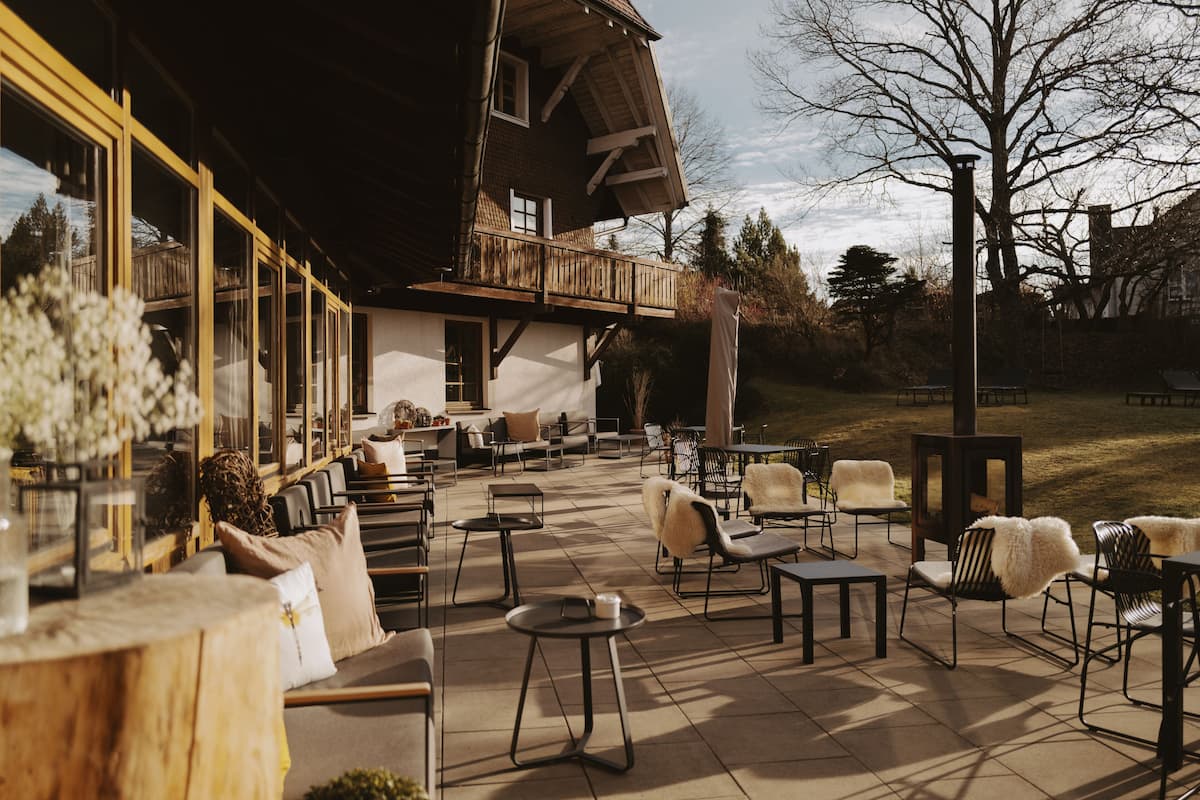 Un patio al aire libre con varias zonas de estar, incluyendo sillas y mesas, y una terraza de madera.
