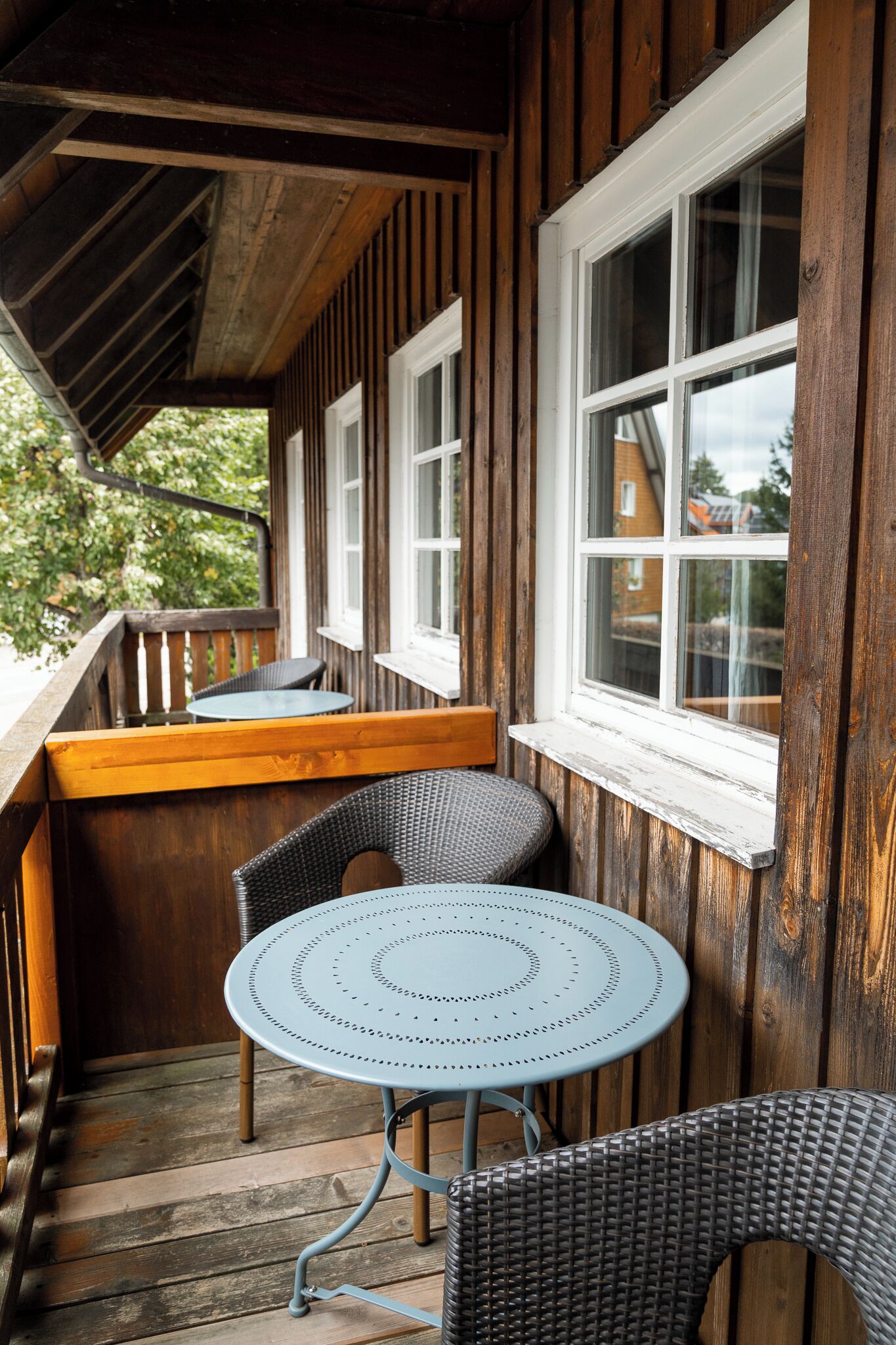 A wooden deck with a round table and two wicker chairs, overlooking a residential area.