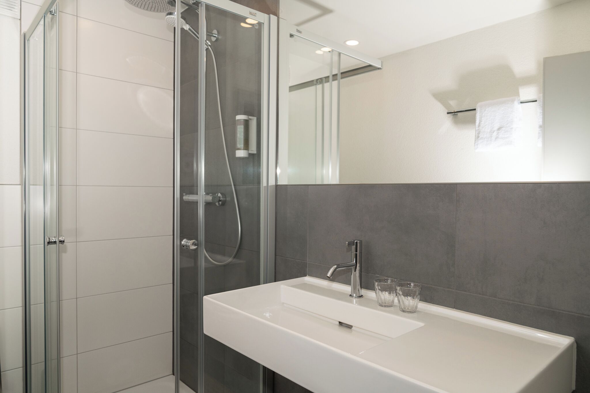 Een moderne badkamer met een glazen douchecabine, een witte wastafel en een spiegel erboven.