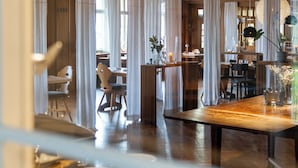 A modern dining area with high ceilings, wooden beams, and a central island with a table and chairs. - Der Hirschen (Sankt Maergen)