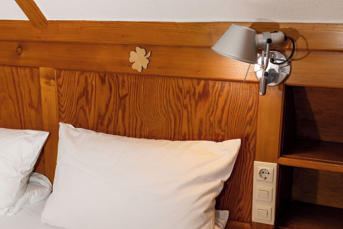 Cabecera de madera con lámpara de noche, mesita de noche de madera y toma de corriente.
