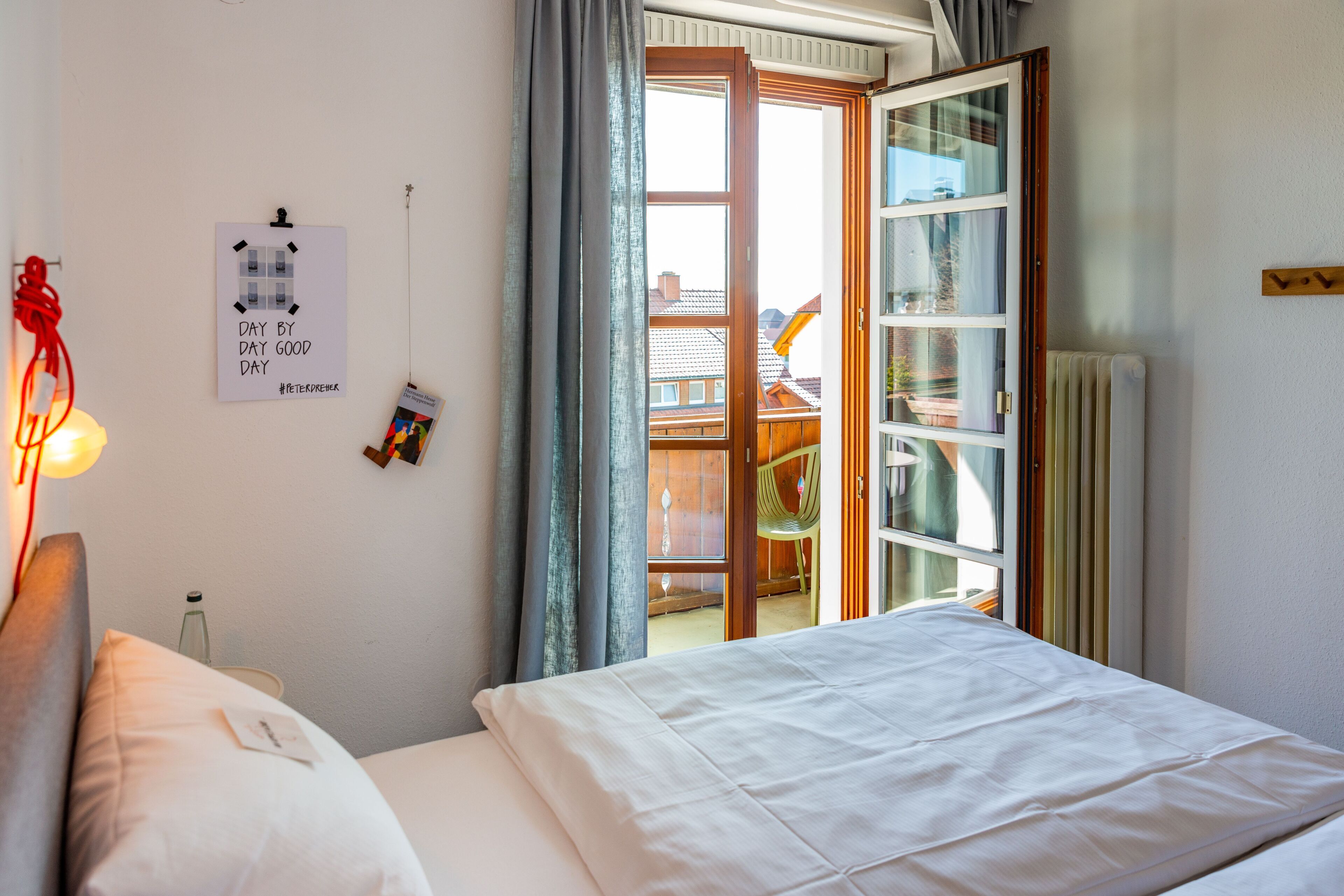 A bedroom with a bed, a bedside table, a lamp, a window with curtains, and a view of the outside.