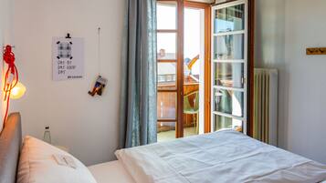 A bedroom with a bed, a bedside table, a lamp, a window with curtains, and a view of the outside.