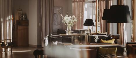 A hotel lobby with a sofa, chairs, a table with a vase, and a lamp.