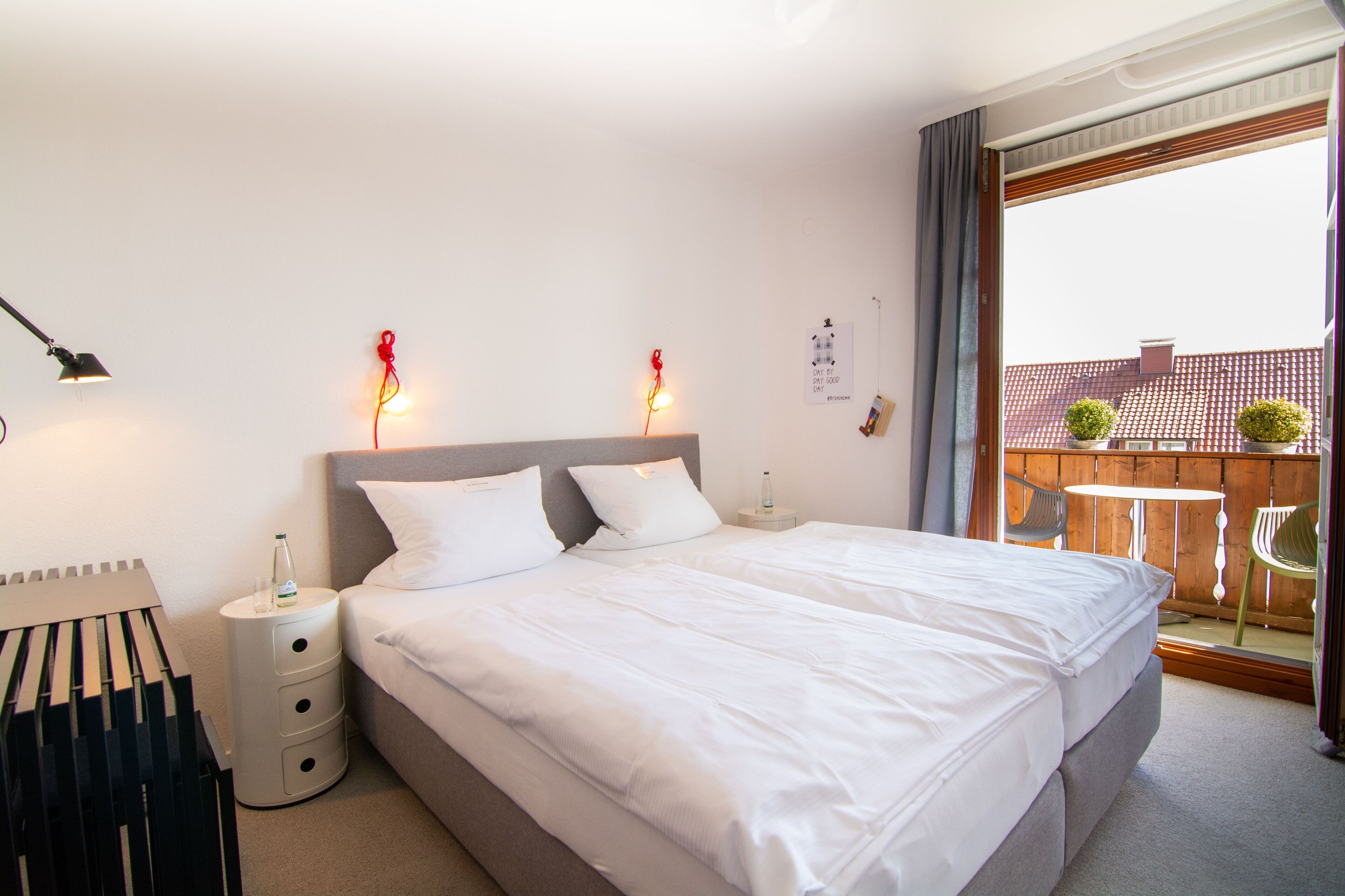 A hotel room with a large bed, a nightstand, a lamp, and a view of the outside balcony.