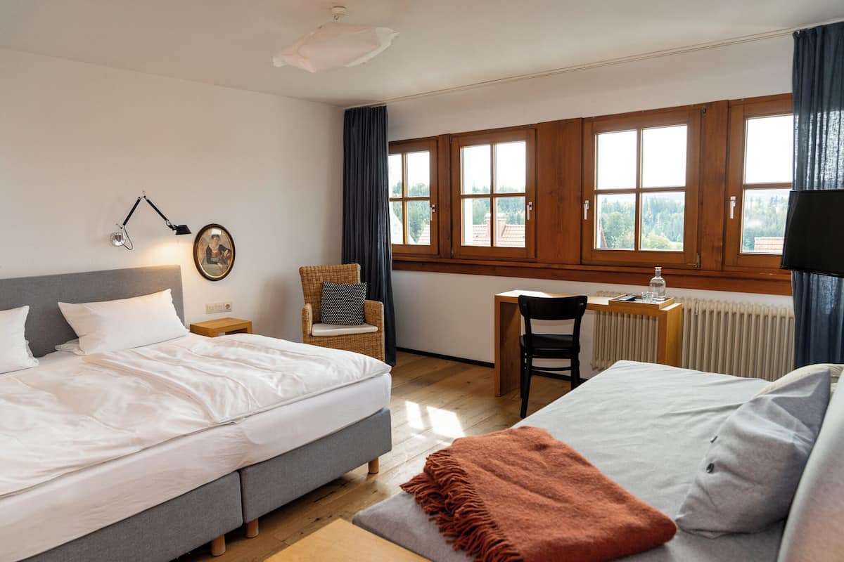Habitación de hotel con dos camas, un escritorio, una silla, una lámpara y una ventana con cortinas.