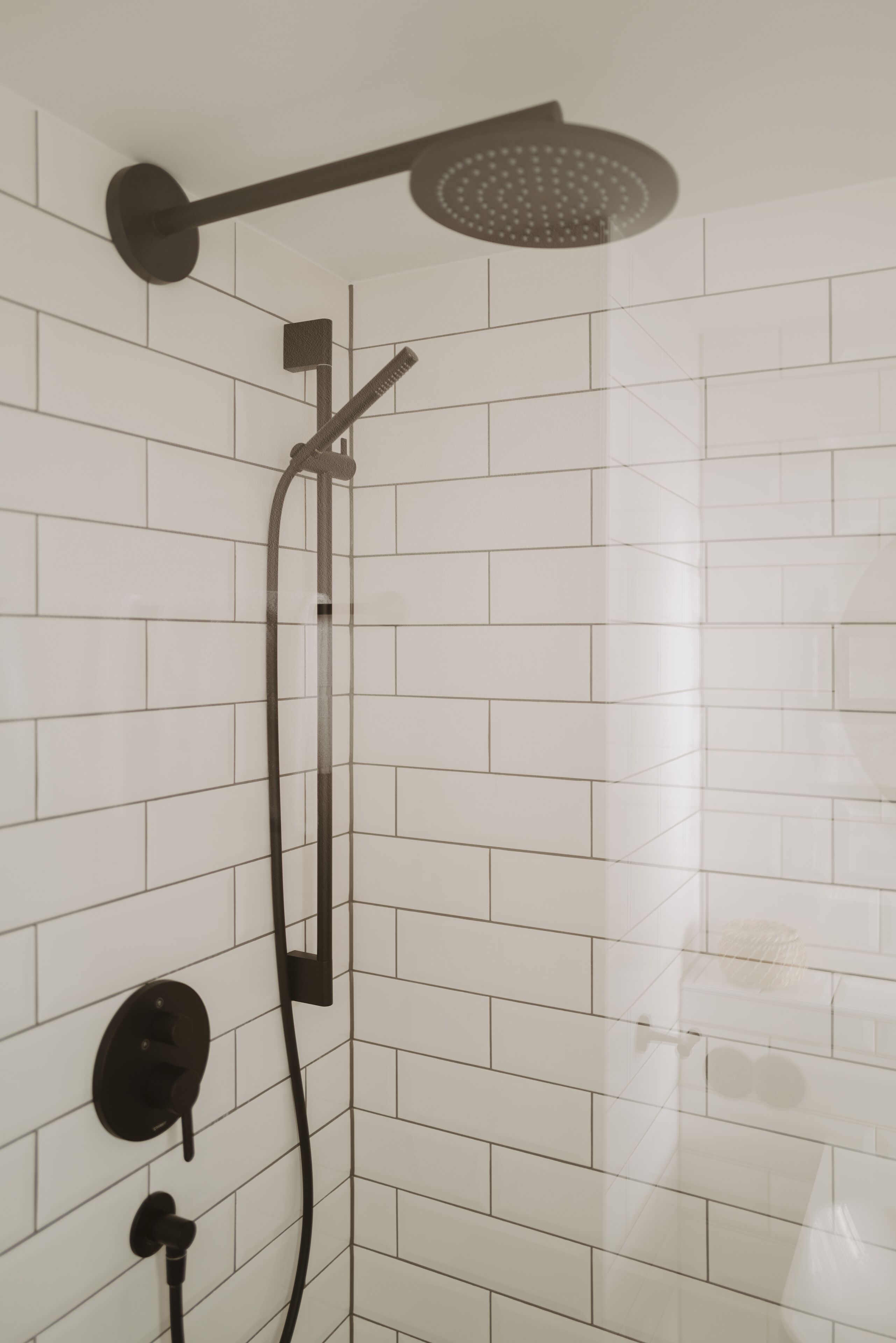 A shower with a handheld showerhead and a wall-mounted control panel.