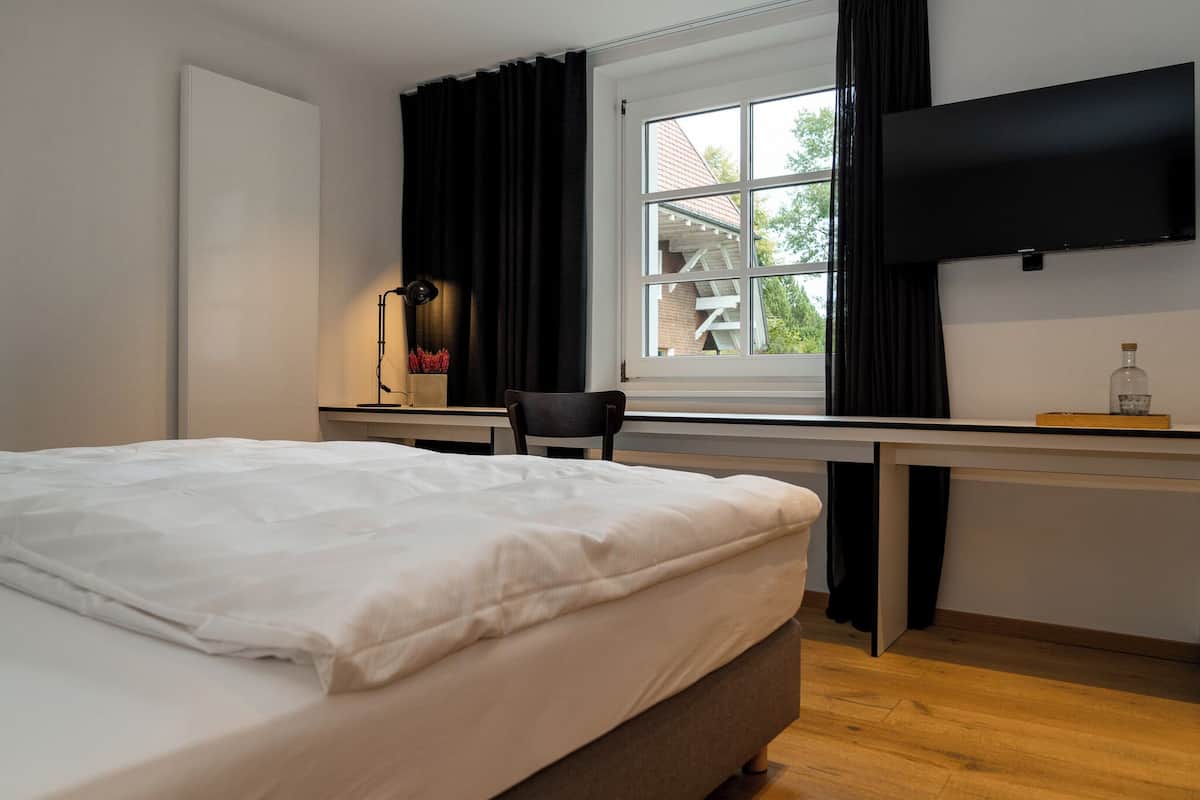 Un dormitorio con cama, escritorio, silla, televisor y ventana con cortinas.