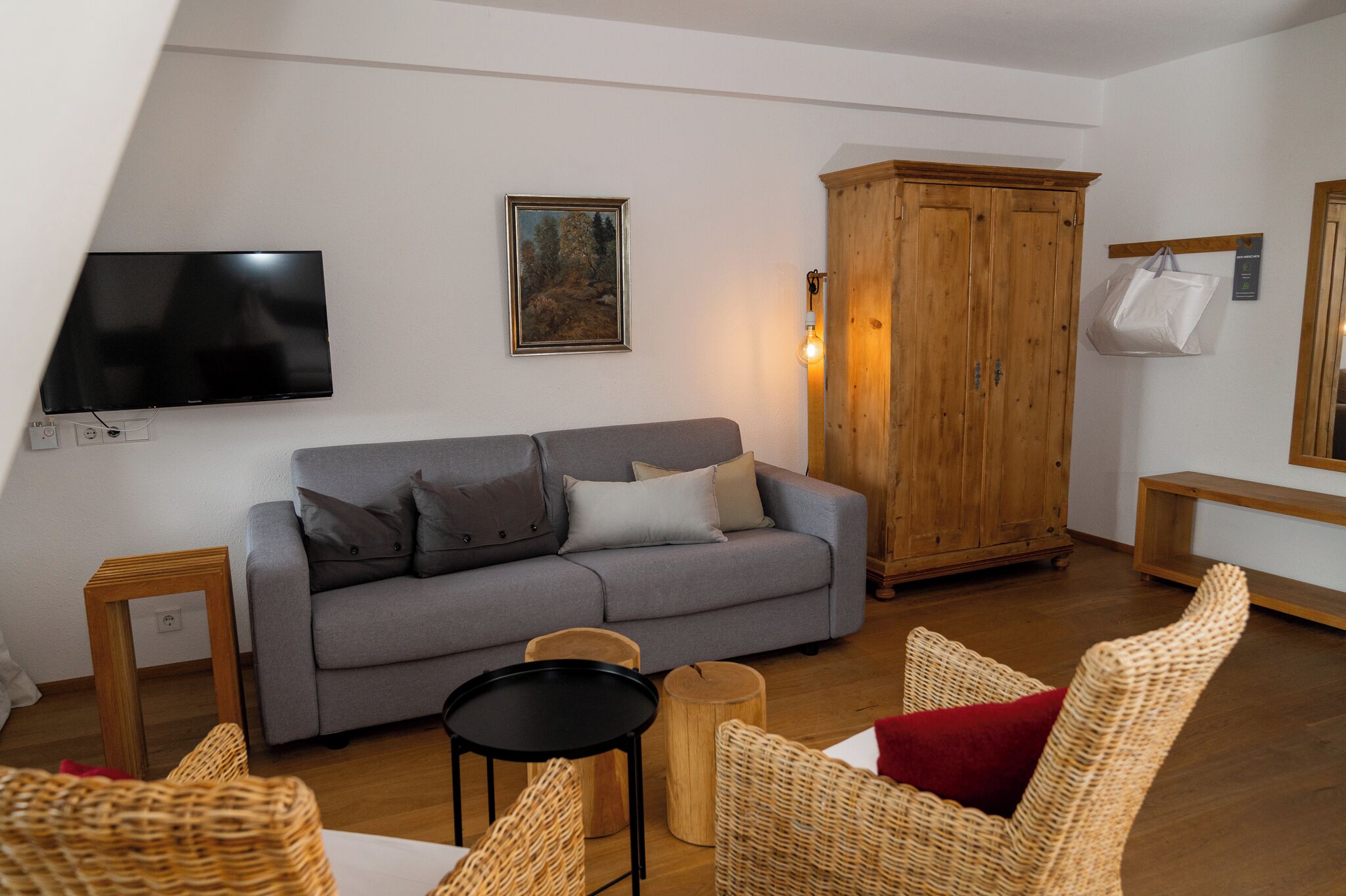 A living room with a grey sofa, wicker chairs, a wooden cabinet, and a flat-screen TV mounted on the wall.