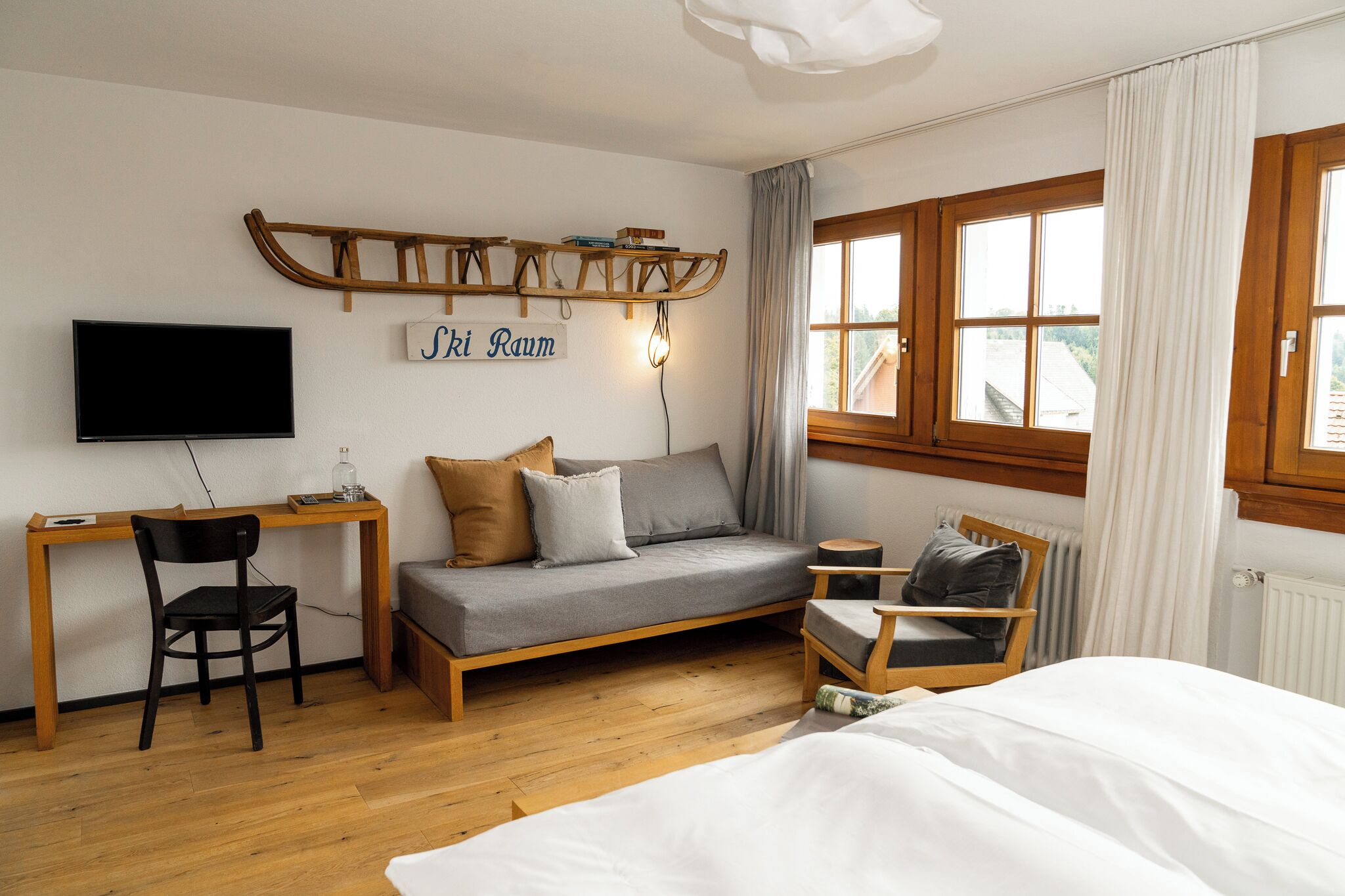 A room with a bed, a desk, a chair, a sofa, a TV, and a window with curtains.